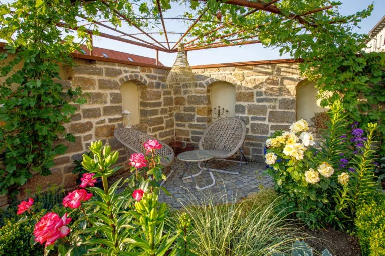 Rückansicht eines romantischen Gartens mit bequemen Möbeln, Blumen und Rankgitter im historischen Steingarten.