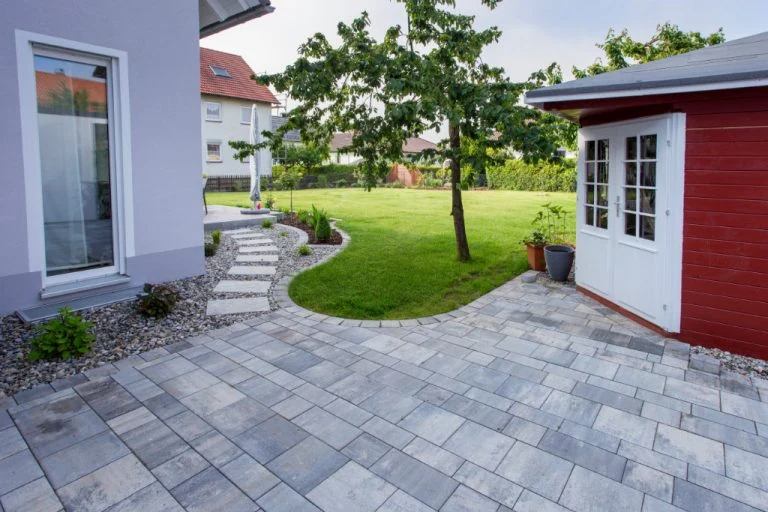 Moderner Garten mit Terrasse und Gartenhaus, gepflegter Rasen und gepflegte Pflanzen.