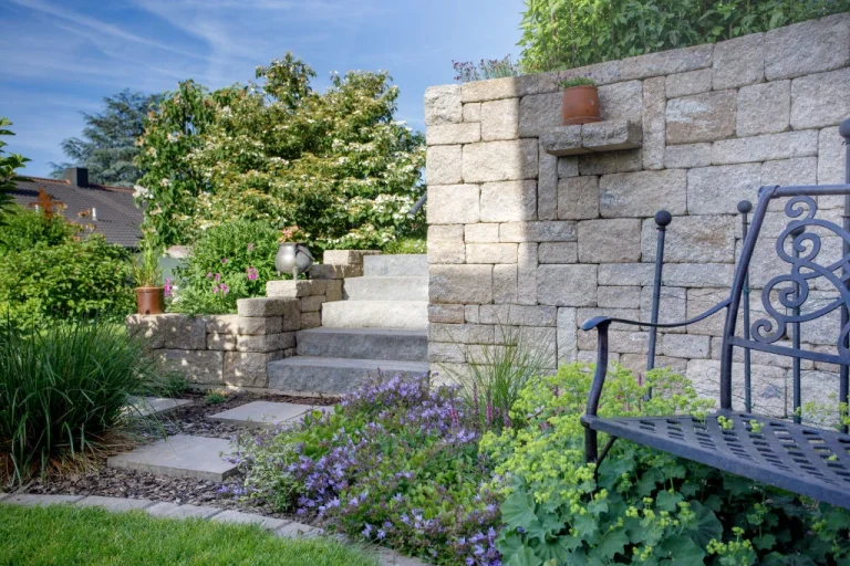 Betonsteinmauer mit integrierter Stufenanlage und Sitzbank in einem liebevoll bepflanzten Garten in der Fränkischen Schweiz, gestaltet von BELLA FLORA GmbH.