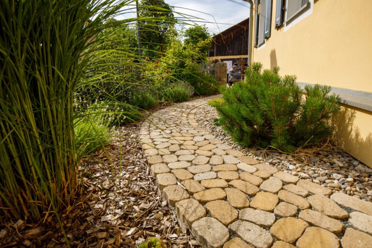 Geschwungener Betonsteinweg mit Kleinpflaster und Kiesstreifen entlang Hausfassade, Gartenweg pflastern in Reuth von BELLA FLORA GmbH.
