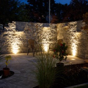 Beleuchtete Natursteinmauer mit gepflastertem Sitzbereich und integrierter Gartenbeleuchtung, Gartenmauerbau und Gartengestaltung in Ebermannstadt von BELLA FLORA GmbH.