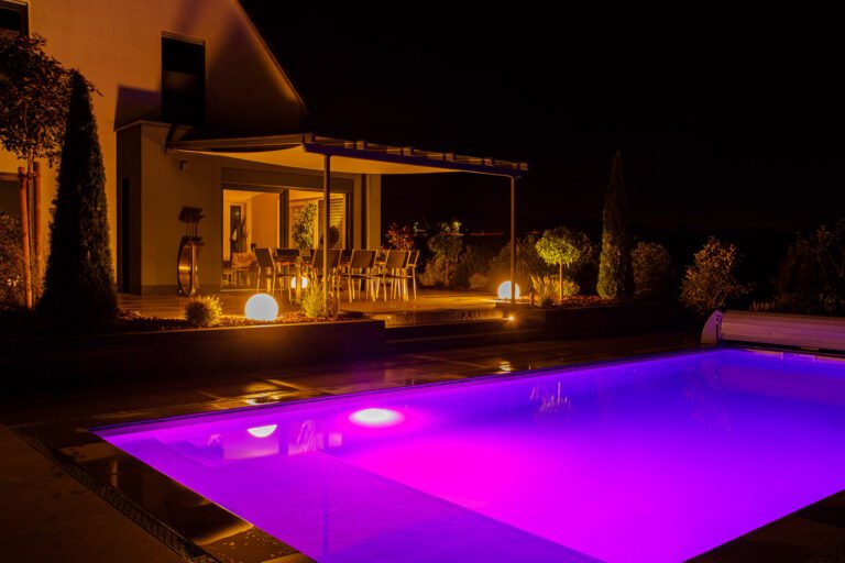 Moderner Pool mit farbiger LED-Unterwasserbeleuchtung, Naturstein-Terrasse, Pergola und professioneller Außenbeleuchtung bei Nacht, Pool- und Gartengestaltung in Buckenhofen von BELLA FLORA GmbH.