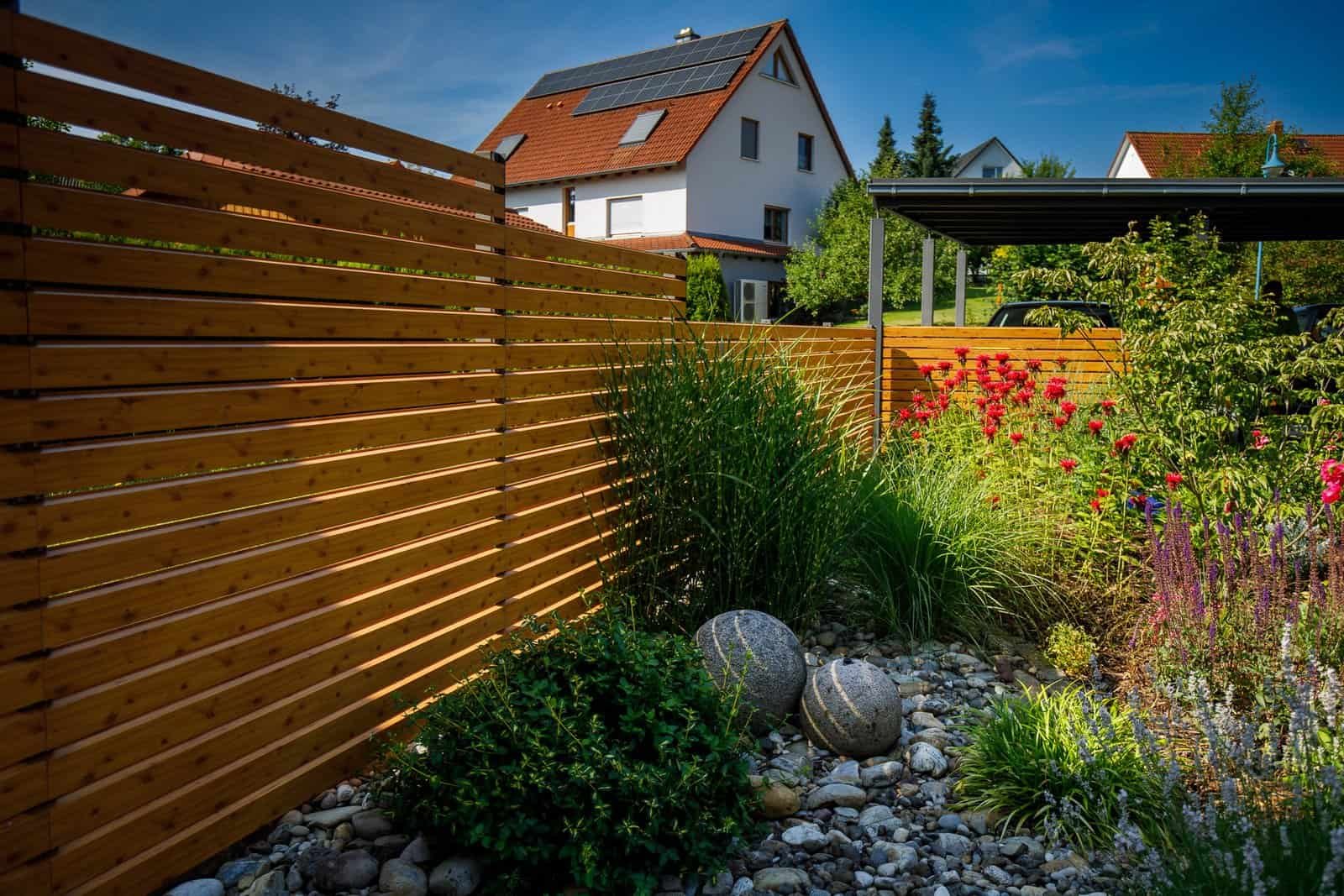 Moderner Holz-Sichtschutzzaun mit horizontalen Lamellen, Staudenbeet, Ziergräsern und Kiesfläche als Gartenabgrenzung, Sichtschutzzaun bauen und Garten anlegen in Heroldsbach von BELLA FLORA GmbH.