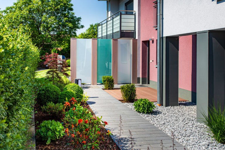 Moderner Sichtschutz aus Glaselementen mit gepflastertem Gartenweg und strukturierter Bepflanzung am Wohnhaus, Sichtschutz bauen im Garten in der Fränkischen Schweiz von BELLA FLORA GmbH.