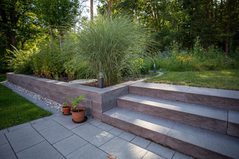 Moderne Terrassenanlage mit breiten Betonblockstufen, niedriger Stützmauer und Staudenbepflanzung mit Ziergräsern, fachgerechter Terrassen- und Mauerbau im Garten in Leutenbach von BELLA FLORA GmbH.
