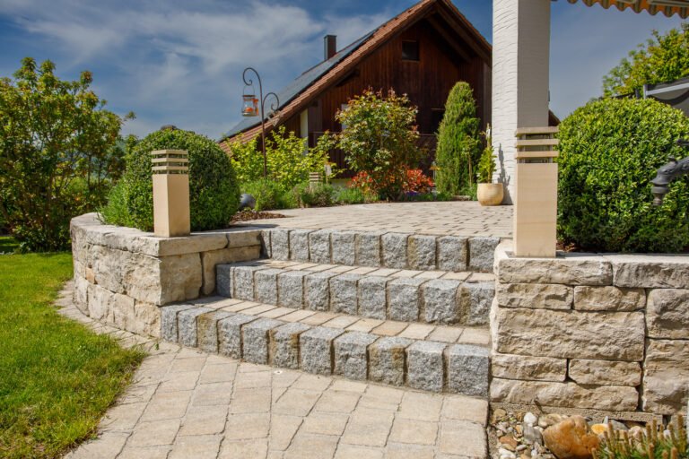Terrassierter Gartenbereich mit Naturstein-Stützmauern, Granitblstufen und gepflasterter Terrasse vor dem Wohnhaus, fachgerechter Terrassen- und Treppenbau in Weilersbach von BELLA FLORA GmbH.