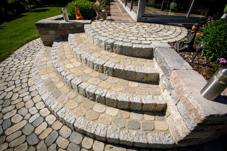 Halbrunde Naturstein-Gartentreppe aus Granit-Kleinsteinpflaster mit integrierter Sitz- und Podestfläche, fachgerechte Pflaster- und Treppenarbeiten im Garten in Heroldsbach von BELLA FLORA GmbH.