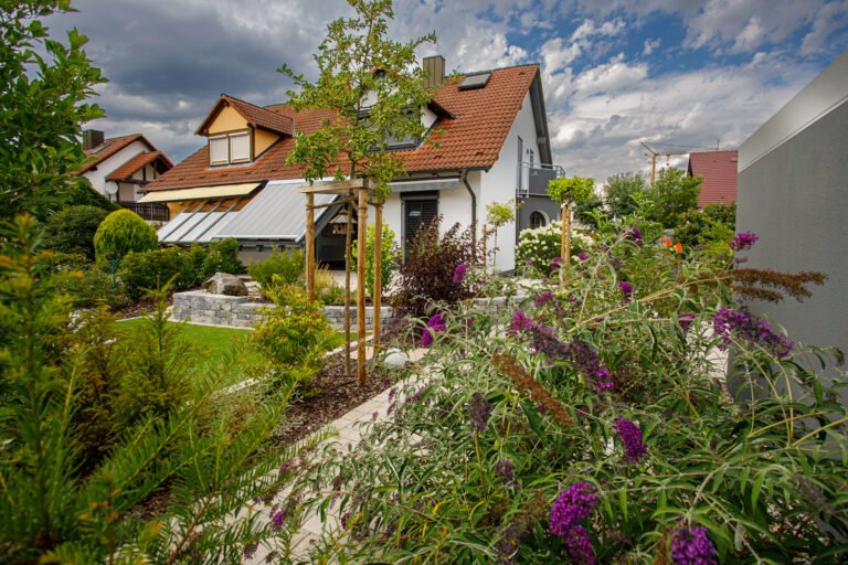 Modern gestalteter Hausgarten mit Staudenbeeten, jungen Bäumen, Rasenfläche und Betonstein-Elementen vor Einfamilienhaus, Gartengestaltung vom Garten- und Landschaftsbau.