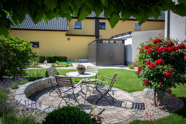 Runder Sitzplatz mit Betonsteinpflaster, gemauerter Sitzmauer, Rasenfläche und Rosenstämmchen im Privatgarten, Garten anlegen in Kersbach von BELLA FLORA GmbH.