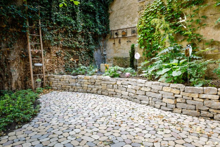 Kleiner Innenhof mit Natursteinmauer, Rundpflaster aus Betonstein und begrünter Wand als fachgerechte Hof- und Gartengestaltung in Buttenheim von BELLA FLORA GmbH.