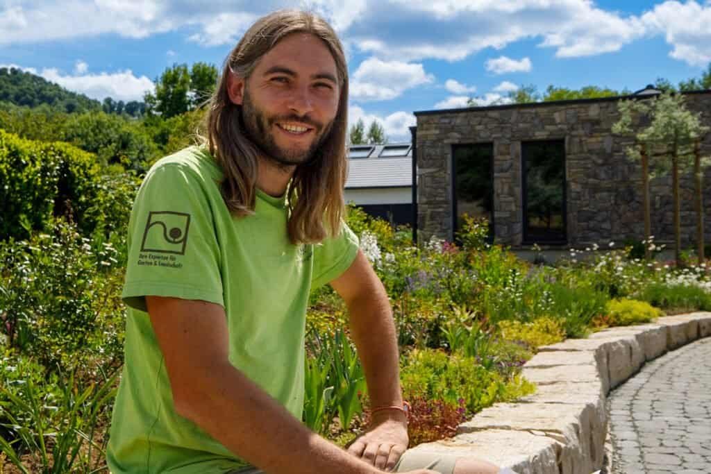 Mitarbeiter von BELLA FLORA an geschwungener Natursteinkante in moderner Staudenpflanzung vor Gartenhaus, professionelle Gartengestaltung und Natursteinarbeiten in Wiesenthau von BELLA FLORA GmbH.