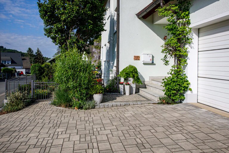 Gepflasterte Hofeinfahrt mit Granitstufen, Kletterpflanzen und Vorgartenbepflanzung – Pflasterarbeiten in Neunkirchen am Brand von BELLA FLORA GmbH.