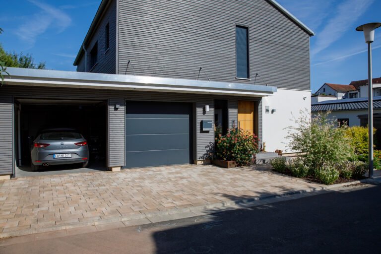 Gepflasterte Einfahrt mit Garage, Hauseingang und angrenzenden Staudenbeeten zur professionellen Vorgartengestaltung in Forchheim von BELLA FLORA GmbH.