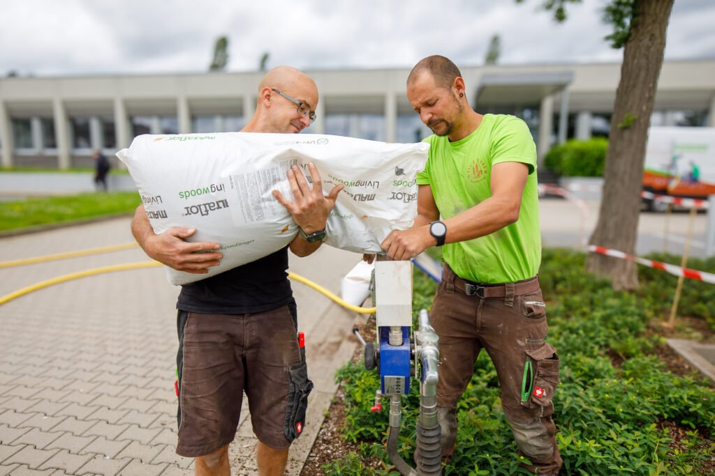 Zwei Landschaftsgärtner beim Befüllen einer Bodeninjektionsanlage mit Substrat, fachgerechte Bodenverbesserung und Wurzelraumbelüftung im öffentlichen Grün durch BELLA FLORA GmbH.