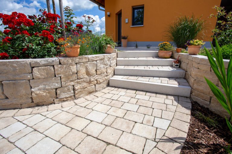 Hauseingangstreppe aus hellen Betonblockstufen mit Kalkstein-Stützmauern, Pflasterbelag und bepflanzten Mauerkronen, Garten- und Landschaftsbau, Kersbach von BELLA FLORA GmbH.