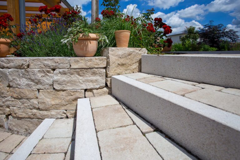 Detailansicht von Naturstein-Treppenanlage mit hellen Blockstufen, Kalkstein-Stützmauer und gepflastertem Podest im Terrassenbereich, Garten- und Landschaftsbau, Burk von BELLA FLORA GmbH.