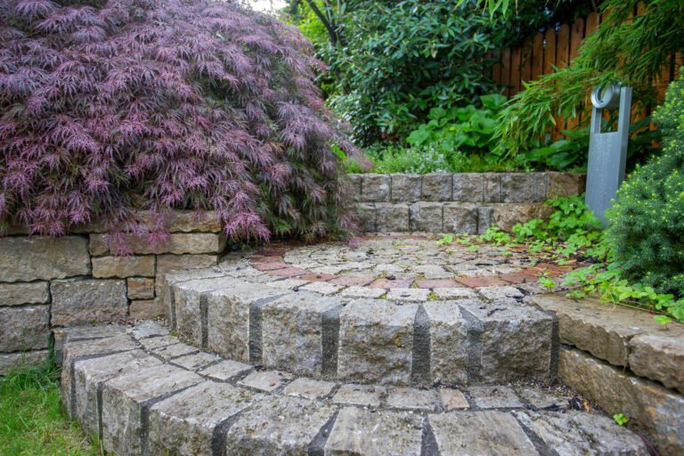 Naturnahe Naturstein-Gartenstufen mit halbrunder Sitzfläche, Kleinpflaster und integrierter Stauden- und Gehölzbepflanzung, Garten- und Landschaftsbau, Buckenhofen von BELLA FLORA GmbH.