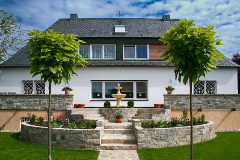 Symmetrische, terrassierte Gartenanlage mit Betonstein-Stützmauern, Mittelachse, Treppenanlage und Brunnen vor Einfamilienhaus, Garten- und Landschaftsbau, Eggolsheim von BELLA FLORA GmbH.