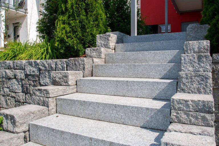 Massive Granit-Außentreppe mit seitlicher Natursteinmauer und klarer Stufenführung am Hauseingang, Garten- und Landschaftsbau, Eggolsheim von BELLA FLORA GmbH.