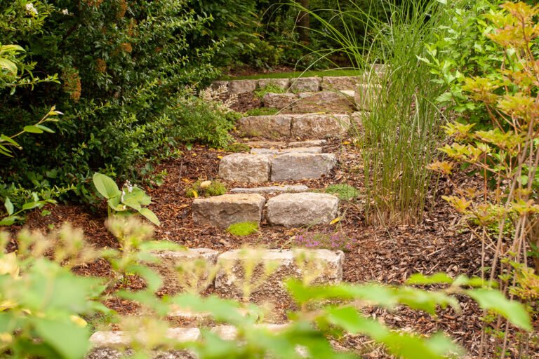 Naturnahe Gartenstufen aus massiven Naturstein-Blockstufen in bepflanztem Hangbereich, Garten- und Landschaftsbau, Ebermannstadt von BELLA FLORA GmbH.