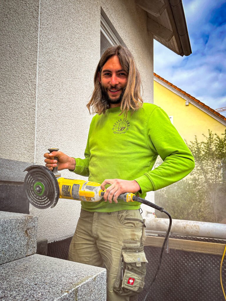 Fachgerechtes Zuschneiden von Granitstufen mit Winkelschleifer bei Treppenbauarbeiten, professionelle Natursteinverarbeitung im Außenbereich in Buckenhofen von BELLA FLORA GmbH.