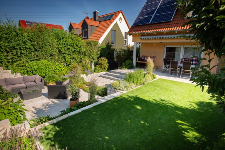 Mehrstufige Gartenanlage mit Terrassenflächen aus Betonplatten, Granitstufen, Bertonsteinmauern, Rasenfläche und strukturierter Staudenbepflanzung im Hausgarten, professionelle Garten- und Landschaftsbauarbeiten in Forchheim von BELLA FLORA GmbH.