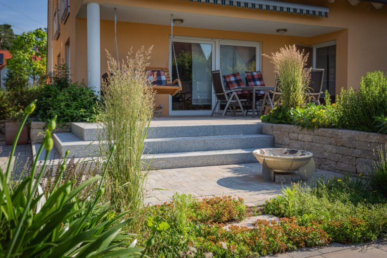 Terrassenanlage mit Granitstufen, Betonpflaster, Feuerstelle und strukturierter Staudenbepflanzung am Wohnhaus, professionelle Terrassen- und Gartenbauarbeiten in Bamberg von BELLA FLORA GmbH.