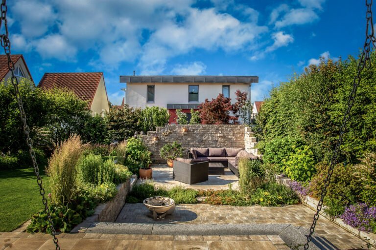 Gartenanlage mit abgesenktem Sitzplatz, Natursteinmauer, Betonplatten und strukturierter Staudenbepflanzung im Hausgarten, professionelle Garten- und Terrassengestaltung in Bamberg von BELLA FLORA GmbH.