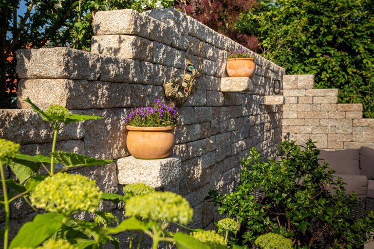 Gestapelte Betonsteinmauer mit integrierten Pflanznischen und Terrakottatöpfen, professioneller Mauerbau und Gartengestaltung in Bamberg von BELLA FLORA GmbH.