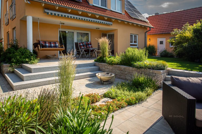 Moderne Gartenterrasse mit Granitstufen, Betonsteinmauer und Staudenbeeten an einem Einfamilienhaus in Bamberg im professionellen Garten- und Landschaftsbau.