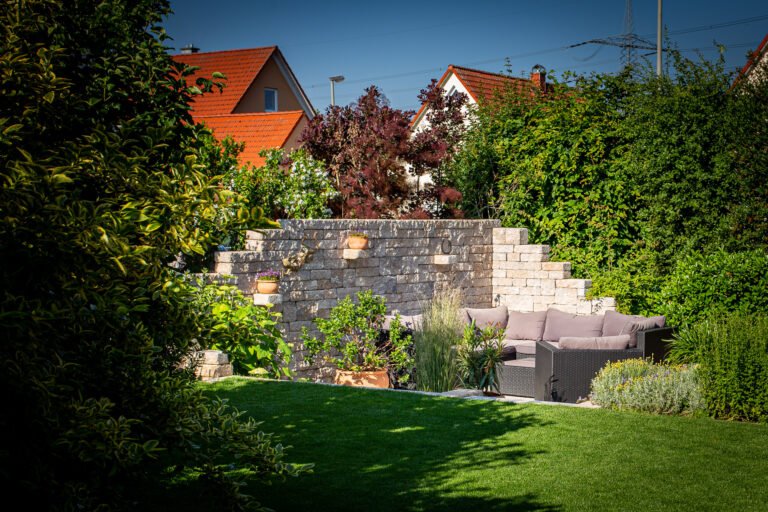 Fertiggestellte Betonstein-Stützmauer mit Rasenfläche und Sitzplatz im privaten Garten, Garten- und Landschaftsbau in Bamberg von BELLA FLORA GmbH.