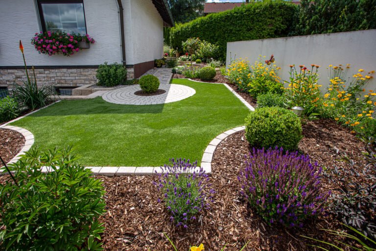 Gepflegte Rasenfläche mit geschwungenen Betonpflaster-Rasenkanten, Staudenbeeten und Pflasterkreis, hochwertige Gartengestaltung und Gartenbau in Reuth von BELLA FLORA GmbH.