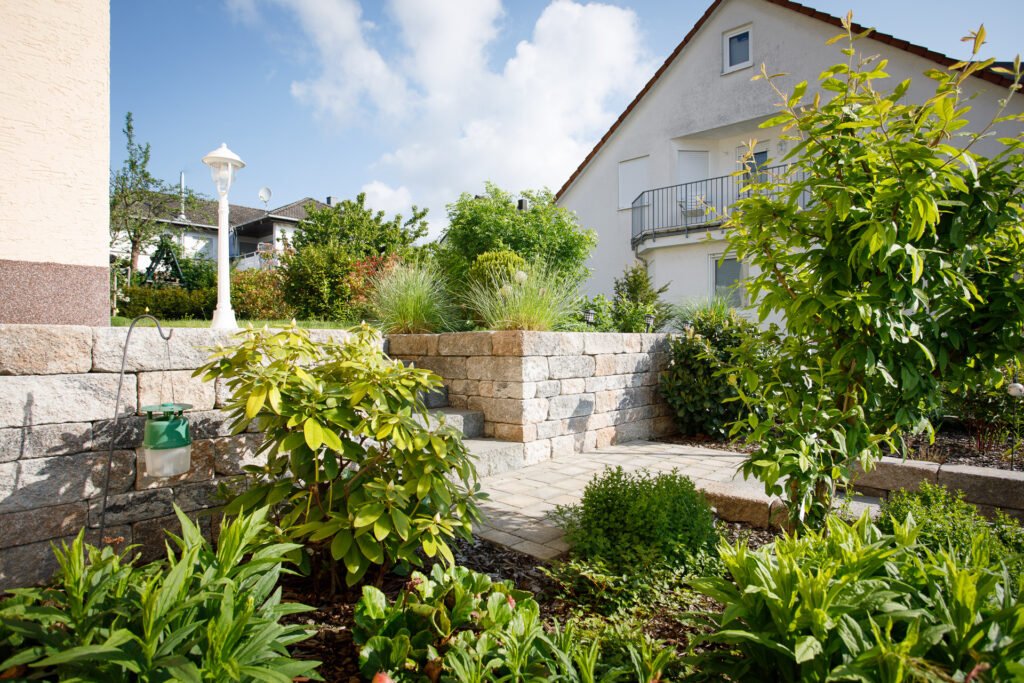 Terrassierte Gartenanlage mit Betonstein-Stützmauer, integrierter Treppenanlage, Pflasterweg und Staudenpflanzung zur Gartengestaltung in Langensendelbach von BELLA FLORA GmbH.