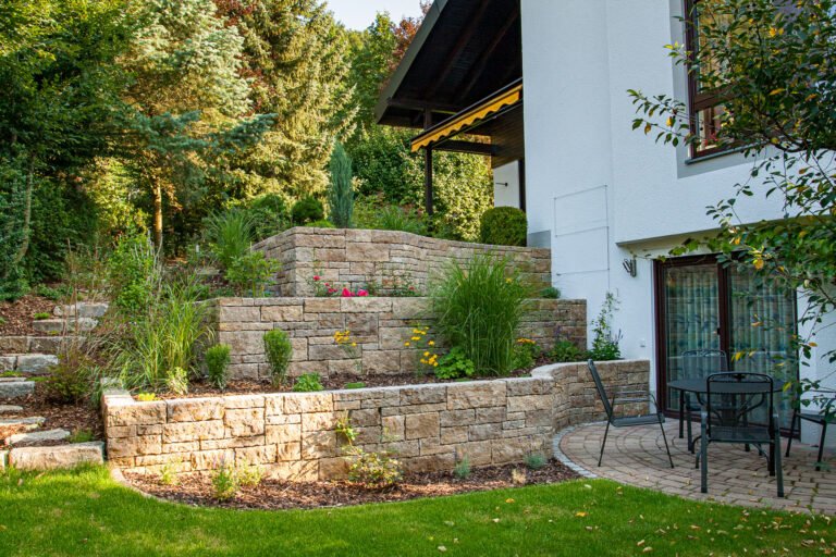 Mehrstufige Naturstein-Stützmauern mit Terrassierung, Stauden- und Ziergräserbepflanzung am Wohnhaus zur Gartengestaltung in Wiesenthau von BELLA FLORA GmbH.