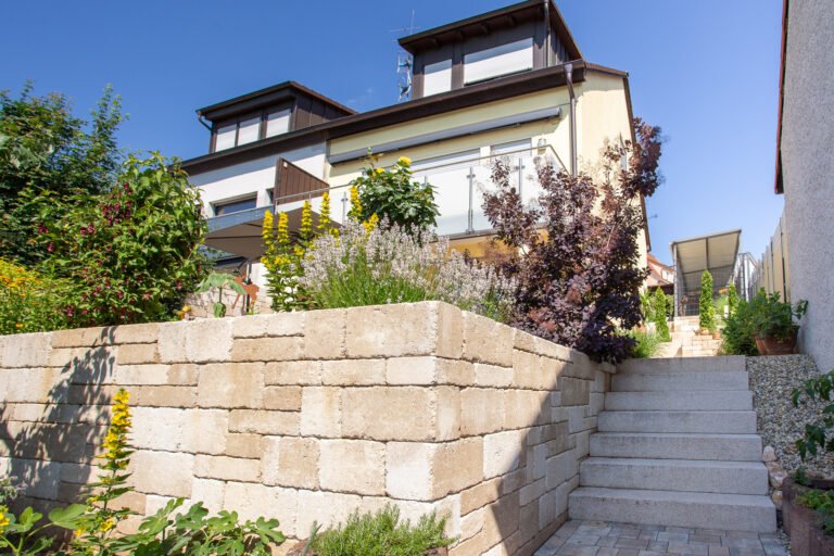 Stützmauer aus Betonstein mit integrierter Granittreppe und Staudenpflanzung zur Gartengestaltung in Hirschaid von BELLA FLORA GmbH.