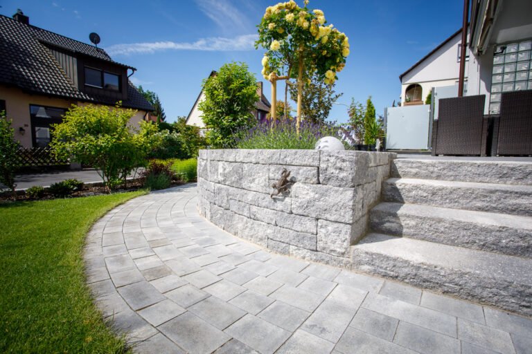 Beton-Hochbeet mit integrierter Treppenanlage, Lavendel- und Gehölzbepflanzung entlang gepflastertem Gartenweg, fachgerechter Garten- und Landschaftsbau in Neunkirchen am Brand von BELLA FLORA GmbH.
