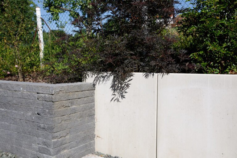 Detailansicht einer modernen Hanggestaltung mit Sichtbeton Stützwinkel und Betonsteinmauer mit Strauchbepflanzung, fachgerechter Garten- und Landschaftsbau in Poxdorf von BELLA FLORA GmbH.