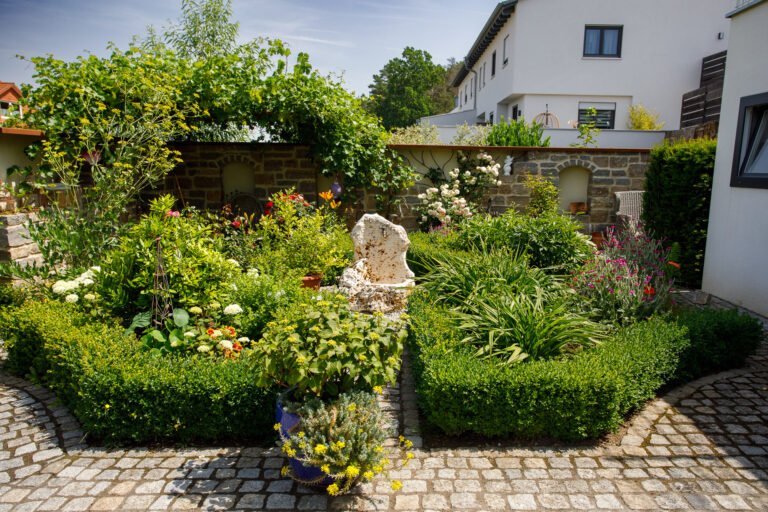 Formal gestalteter Innenhofgarten mit geschnittenen Buchshecken, Natursteinpflaster und zentralem Steinelement als professionelle Gartengestaltung in Forchheim von BELLA FLORA GmbH.