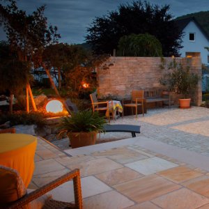 Großzügige Naturstein-Terrasse mit Sitzbereich, Feuerstelle und stimmungsvoller Gartenbeleuchtung, Terrassenbau und Gartengestaltung in der Fränkischen Schweiz von BELLA FLORA GmbH.