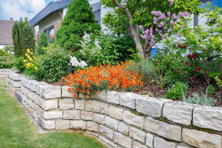 Naturstein-Stützmauer mit üppiger Stauden- und Gehölzbepflanzung im Vorgarten eines Wohnhauses, fachgerechter Garten- und Landschaftsbau in Buckenhofen von BELLA FLORA GmbH.
