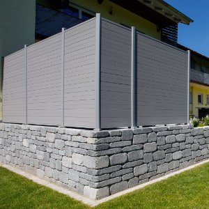 Betonsteinmauer mit aufgesetztem Sichtschutzzaun zur Grundstückseinfassung im Rahmen der Gartengestaltung in Streitberg von BELLA FLORA GmbH.