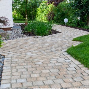 Geschwungener Gartenweg aus Granitpflaster mit sauberer Einfassung und angrenzender Rasenfläche als professionelle Pflasterarbeit in Streitberg von BELLA FLORA GmbH.