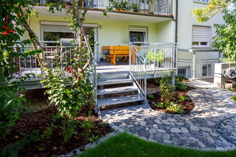 Fertiggestellte Gartenterrasse mit Stahlkonstruktion, Treppe und geschwungenem Betonsteinweg im Garten- und Landschaftsbau in Weilersbach von BELLA FLORA GmbH.