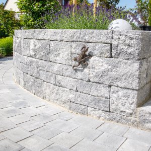Geschwungene Betonsteinmauer mit Betonpflasterweg im Vordergrund, Stützmauer bauen in Pinzberg von BELLA FLORA GmbH.