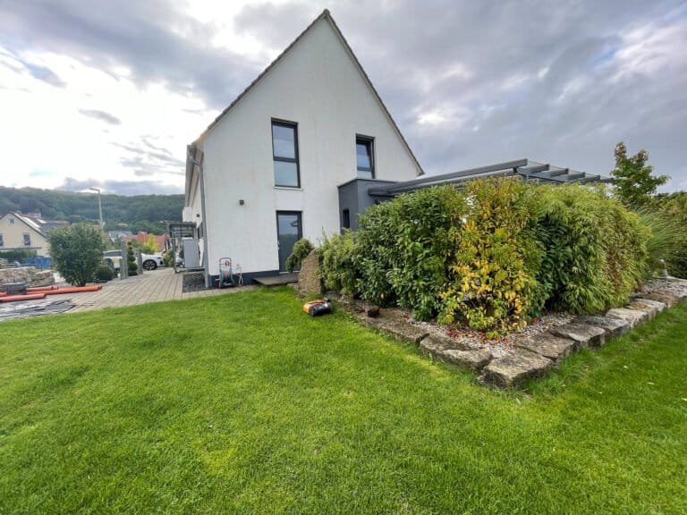 Modernes Einfamilienhaus mit Rasenfläche, Naturstein-Hochbeet und dichter Heckenbepflanzung als Gartengestaltung in Ebermannstadt von BELLA FLORA GmbH.