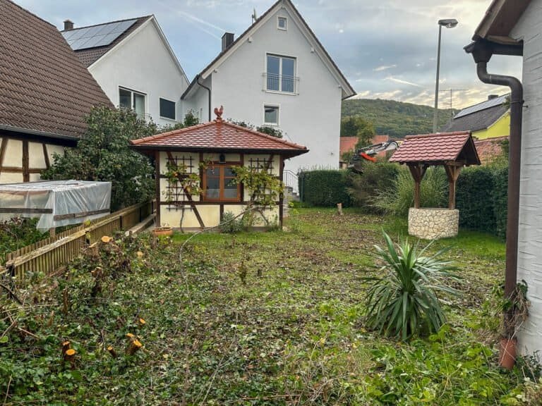 In die Jahre gekommener Hausgarten mit Rasenfläche, Gartenhaus und Brunnen als Gartensanierung in Pottenstein von BELLA FLORA GmbH.