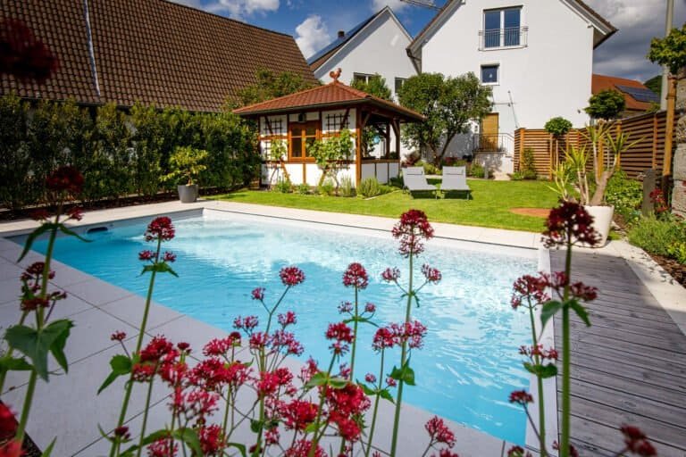 Rechteckiger Swimmingpool mit Holzdeck, großformatiger Terrassenbefestigung und Gartenpavillon im Privatgarten in Kersbach von BELLA FLORA GmbH.