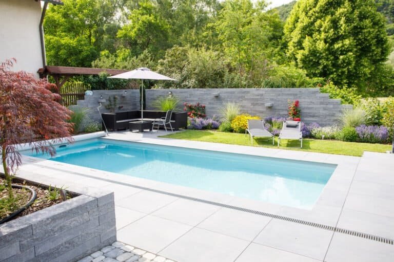 Moderner Rechteckpool mit Betonstein-Terrasse, Sichtschutzmauer und Staudenbepflanzung als Poolbau im Privatgarten in Poxdorf von BELLA FLORA GmbH.