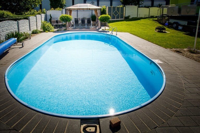 Ovaler Gartenpool mit Pflasterumrandung, Rasenfläche und Pavillon als Poolbau im Privatgarten in Pinzberg von BELLA FLORA GmbH.