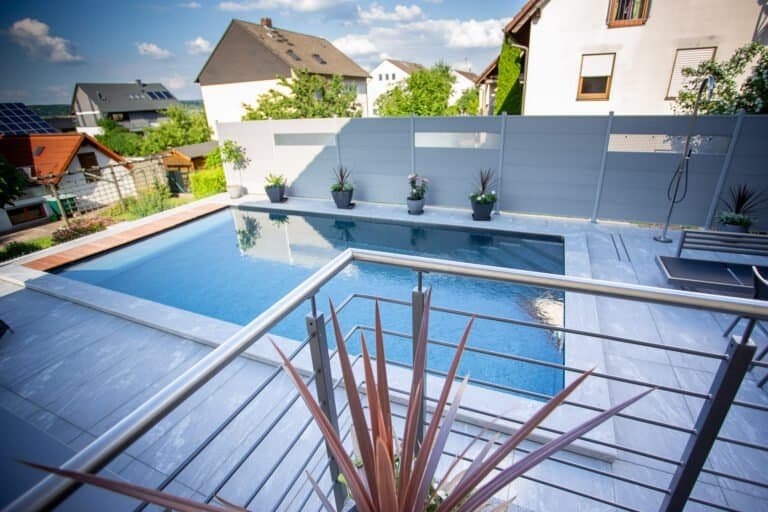 Moderner Gartenpool mitKeramik-Terrasse, Sichtschutzwand und Edelstahlelementen als Poolbau in Kirchehrenbach von BELLA FLORA GmbH.